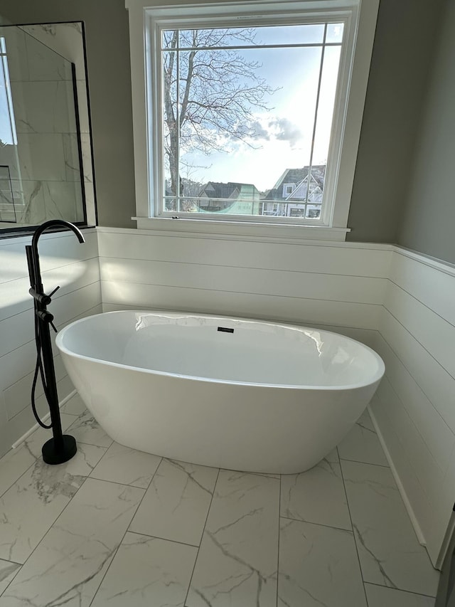 bathroom featuring a freestanding tub, marble finish floor, and a wainscoted wall