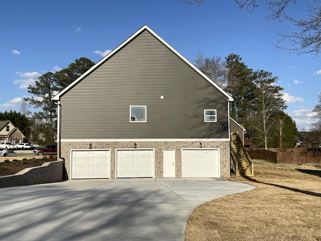 view of side of property featuring brick siding, driveway, an attached garage, and stairway