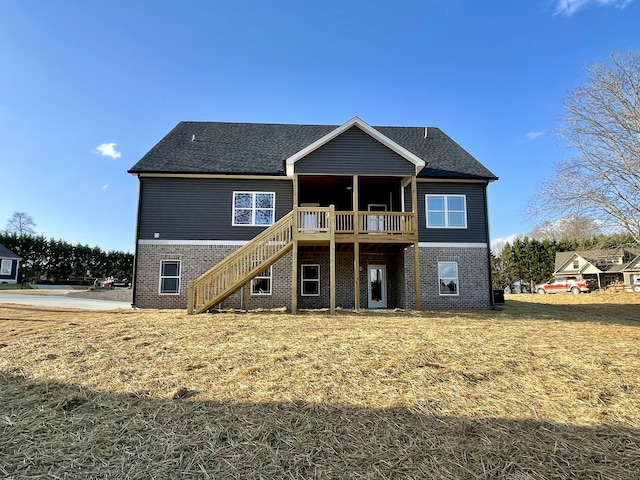 rear view of property with roof with shingles, brick siding, stairway, and a deck
