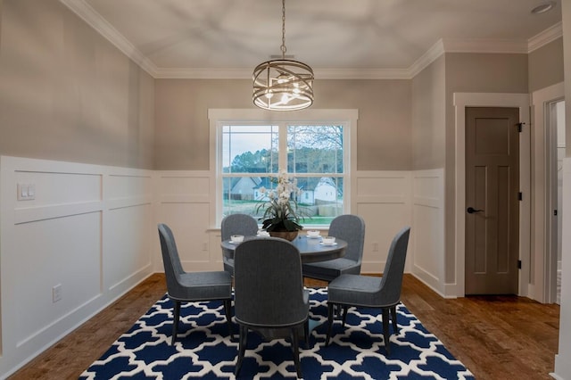dining space featuring dark wood-style flooring, a decorative wall, a notable chandelier, and ornamental molding