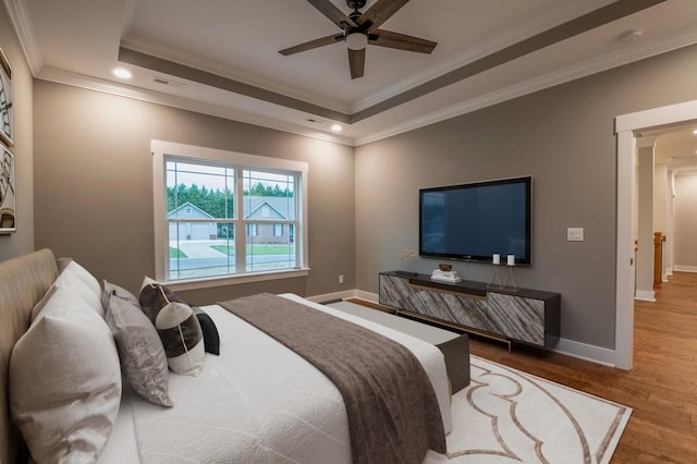 bedroom with a tray ceiling, baseboards, crown molding, and wood finished floors
