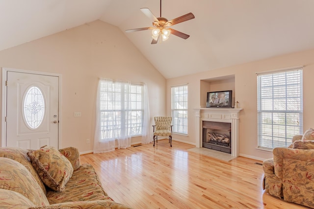 living area featuring high vaulted ceiling, a fireplace with flush hearth, light wood-style floors, and ceiling fan