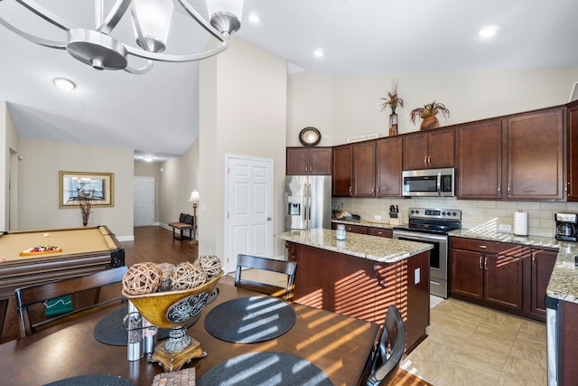 kitchen featuring decorative backsplash, high vaulted ceiling, light stone countertops, and stainless steel appliances