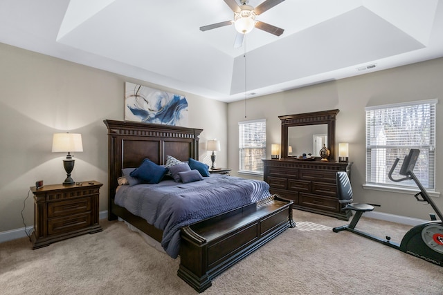 carpeted bedroom featuring a ceiling fan, a tray ceiling, baseboards, and visible vents