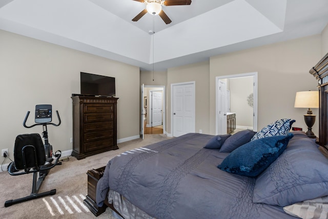 bedroom featuring ceiling fan, baseboards, a tray ceiling, light carpet, and ensuite bath