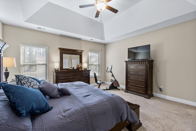 bedroom with visible vents, ceiling fan, baseboards, a tray ceiling, and light carpet