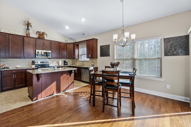 kitchen featuring dark brown cabinets, vaulted ceiling, decorative backsplash, appliances with stainless steel finishes, and a notable chandelier