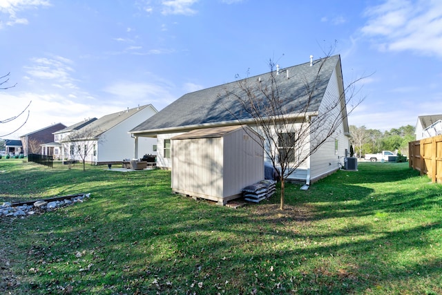 rear view of property with a storage unit, a lawn, central AC, fence, and an outdoor structure