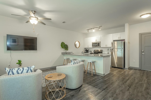 interior space with a kitchen bar, appliances with stainless steel finishes, a peninsula, and dark wood finished floors