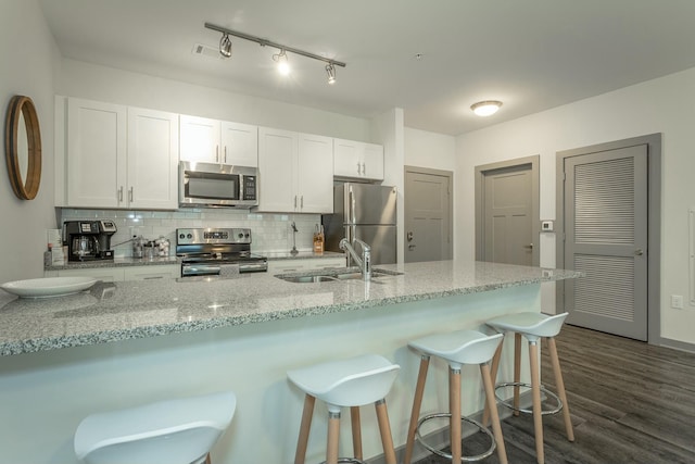 kitchen with dark wood-type flooring, decorative backsplash, stainless steel appliances, white cabinetry, and a sink