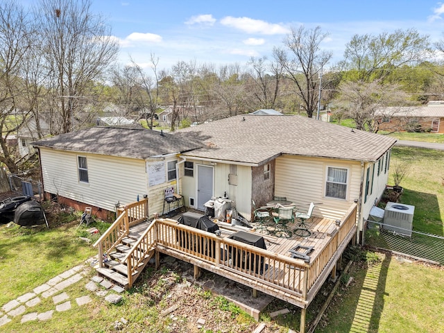rear view of house with a shingled roof, a deck, and a lawn