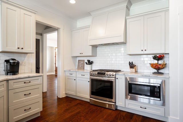 kitchen featuring tasteful backsplash, light stone countertops, dark wood finished floors, custom range hood, and appliances with stainless steel finishes