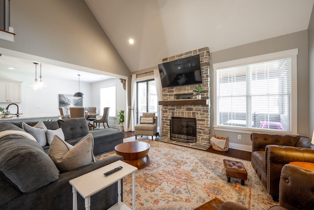 living area with a stone fireplace, high vaulted ceiling, wood finished floors, and a healthy amount of sunlight