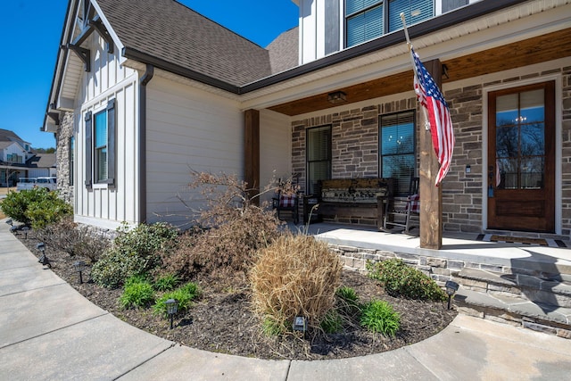 property entrance featuring stone siding, a porch, and roof with shingles