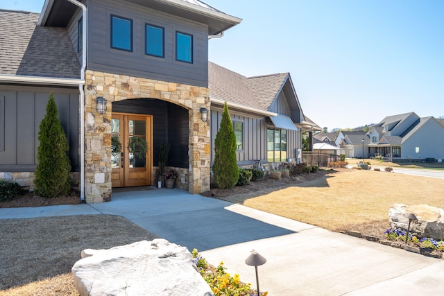 exterior space with stone siding, french doors, a residential view, and roof with shingles