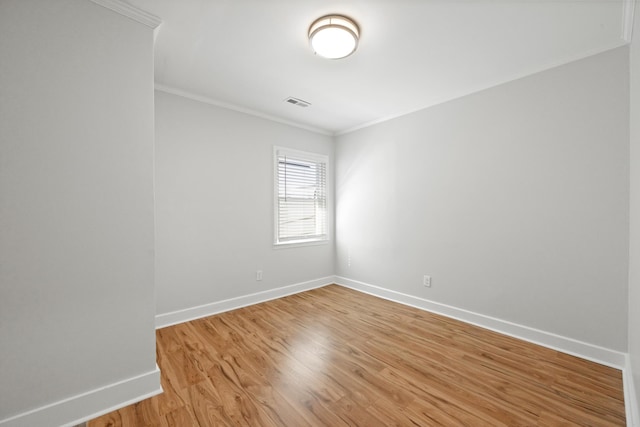 spare room featuring visible vents, light wood-type flooring, crown molding, and baseboards