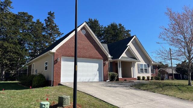 ranch-style house featuring driveway, brick siding, an attached garage, and a front yard