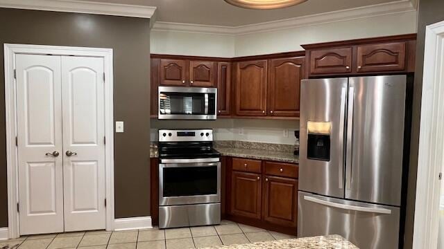 kitchen featuring stone counters, stainless steel appliances, crown molding, baseboards, and light tile patterned flooring