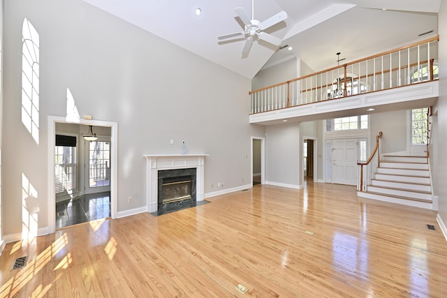 unfurnished living room with light wood-type flooring, a fireplace, a ceiling fan, visible vents, and high vaulted ceiling