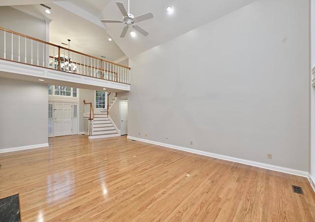 unfurnished living room with light wood-type flooring, a ceiling fan, stairs, visible vents, and high vaulted ceiling