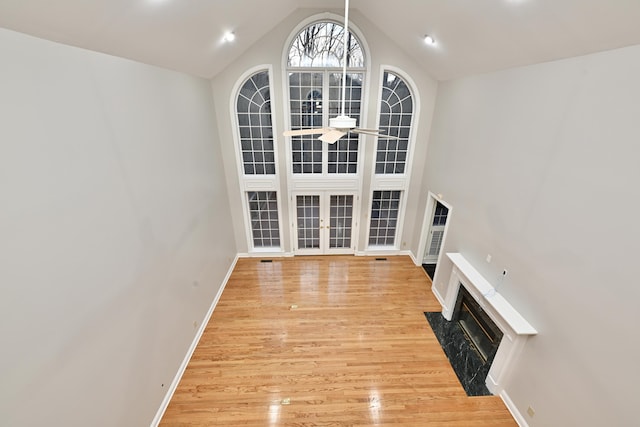 unfurnished living room featuring ceiling fan, light wood-type flooring, vaulted ceiling, a premium fireplace, and baseboards