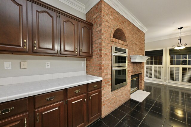 kitchen with stainless steel double oven, dark brown cabinetry, ornamental molding, and dark tile patterned flooring