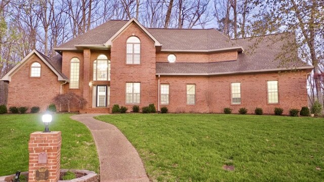 view of front of house featuring a shingled roof, a front yard, and brick siding