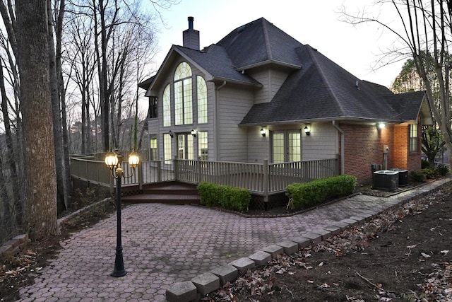 back of property featuring a wooden deck, a chimney, roof with shingles, brick siding, and french doors