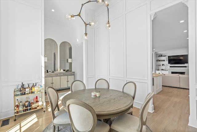 dining room with recessed lighting, crown molding, light wood-style floors, visible vents, and a decorative wall