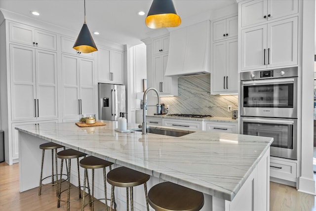 kitchen featuring custom exhaust hood, white cabinets, a sink, light wood-style floors, and stainless steel appliances