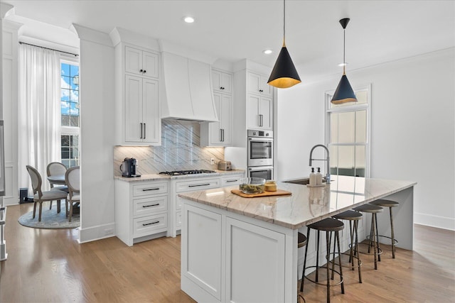 kitchen featuring a sink, gas stovetop, double oven, custom range hood, and decorative backsplash