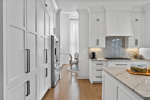 kitchen featuring tasteful backsplash, white cabinets, light stone counters, premium range hood, and light wood finished floors