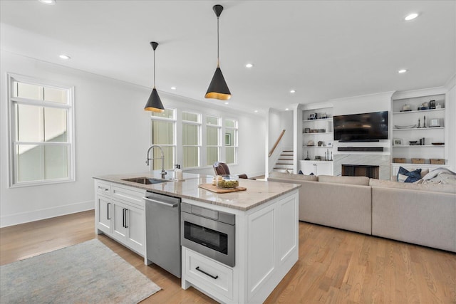 kitchen with an island with sink, light wood-style flooring, white cabinets, appliances with stainless steel finishes, and a sink