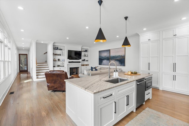 kitchen featuring light wood-type flooring, a kitchen island with sink, a sink, and white cabinetry