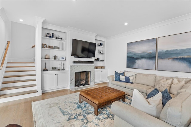 living area with crown molding, a fireplace with flush hearth, recessed lighting, stairs, and light wood finished floors