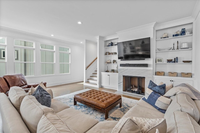 living room with crown molding, baseboards, light wood-type flooring, and stairway