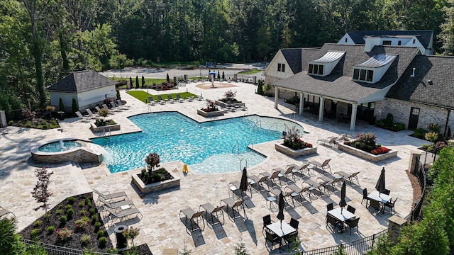 community pool with an outbuilding, a hot tub, a patio, fence, and a wooded view
