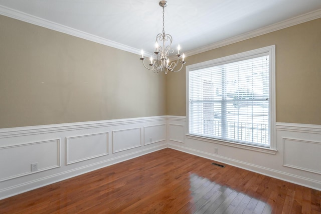 empty room with visible vents, a notable chandelier, ornamental molding, wood finished floors, and wainscoting