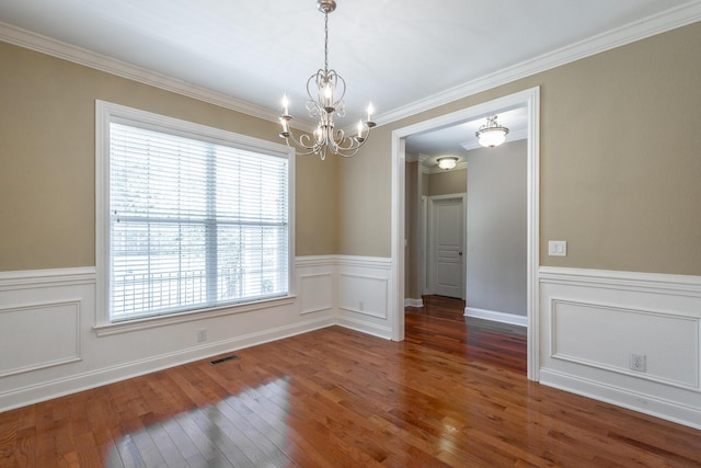 unfurnished dining area featuring visible vents, a wainscoted wall, ornamental molding, an inviting chandelier, and hardwood / wood-style flooring