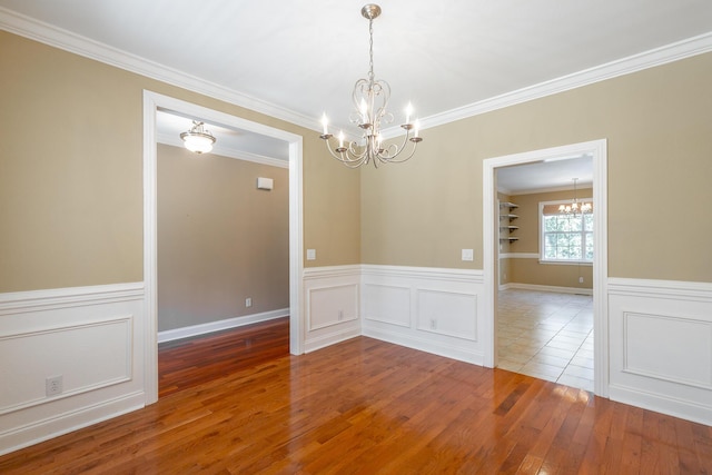 spare room featuring a wainscoted wall, a notable chandelier, crown molding, and hardwood / wood-style flooring