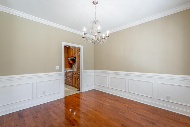 spare room with a wainscoted wall, an inviting chandelier, light wood-style flooring, and ornamental molding