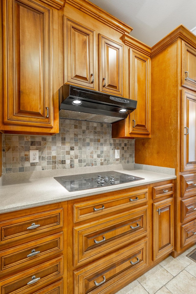 kitchen with light countertops, under cabinet range hood, black electric stovetop, brown cabinets, and backsplash