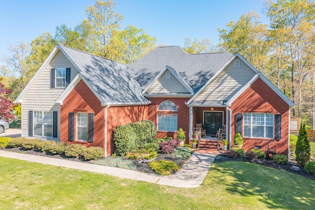 view of front of property featuring covered porch, brick siding, a front yard, and roof with shingles