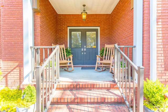 entrance to property with french doors, covered porch, and brick siding