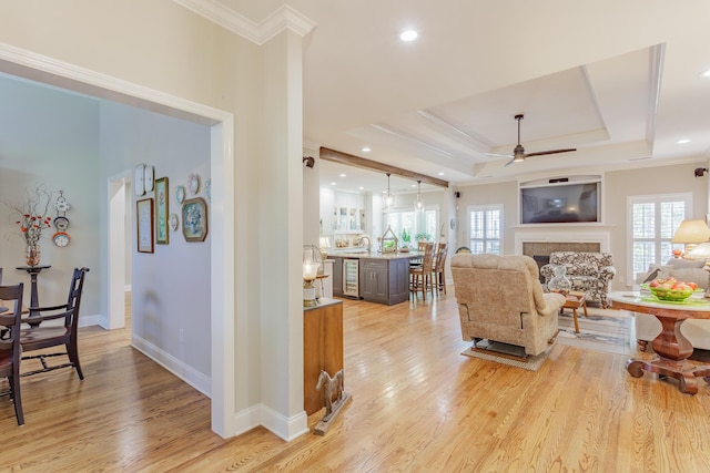 living area with ceiling fan, a fireplace, light wood-style flooring, baseboards, and ornamental molding