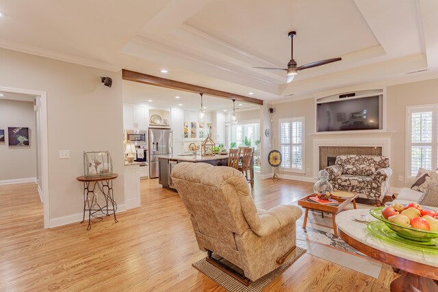 living area with crown molding, ceiling fan, a fireplace, and light wood-type flooring