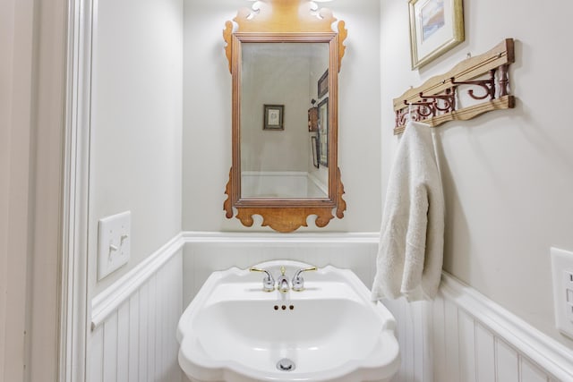 bathroom with a sink, a decorative wall, and a wainscoted wall