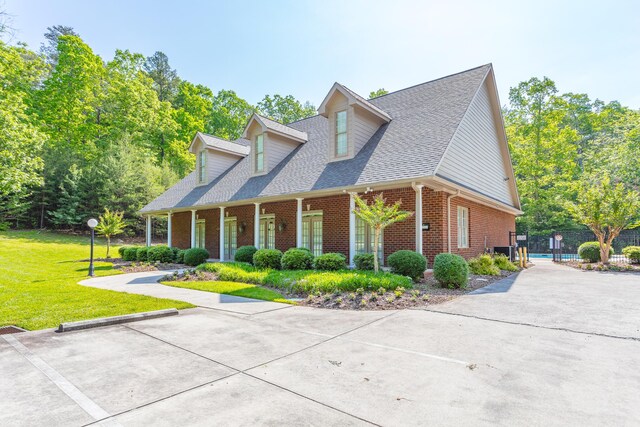 view of front facade with roof with shingles, fence, a front lawn, brick siding, and a porch