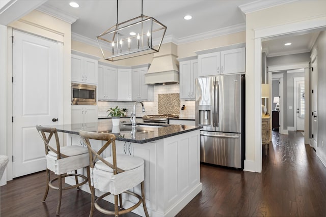 kitchen featuring an island with sink, ornamental molding, a sink, stainless steel appliances, and dark wood-style flooring