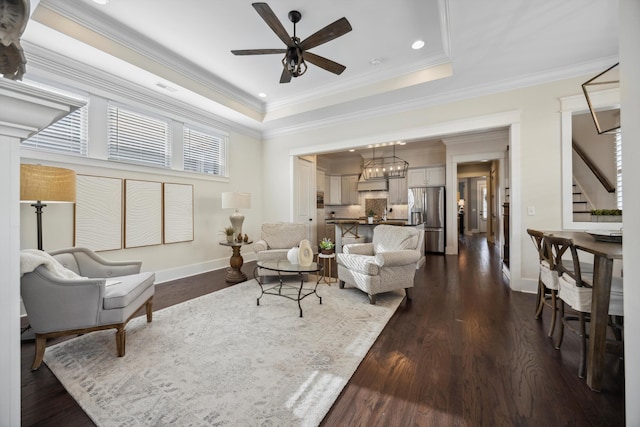 living room with stairs, a tray ceiling, dark wood-style flooring, and a ceiling fan
